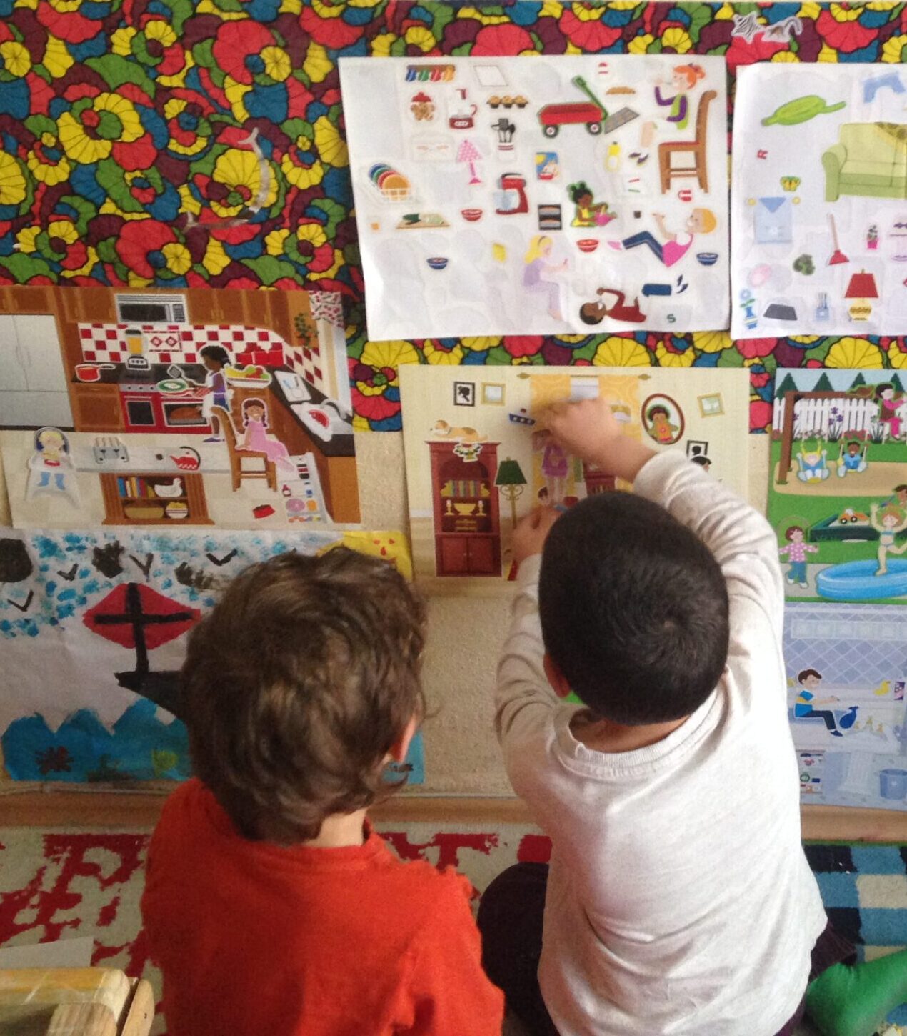 Two young children from behind looking at a colourful learning wall display in a home education setting