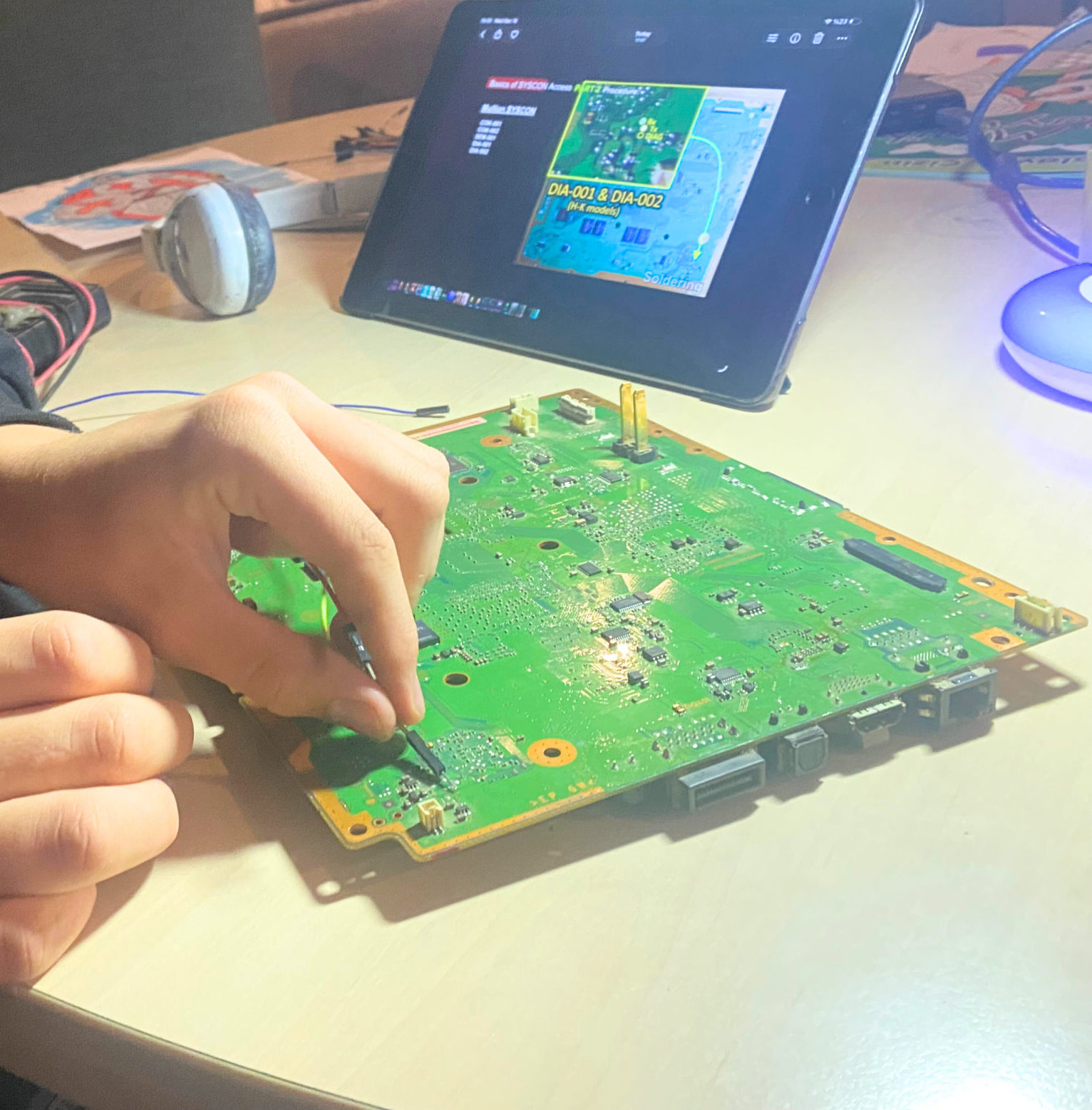 Teenager repairing a circuit board at home, following a tutorial on a tablet — self-directed learning during a home-ed study week