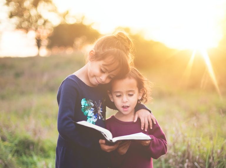 girl's left hand wrap around toddler while reading book during golden hour