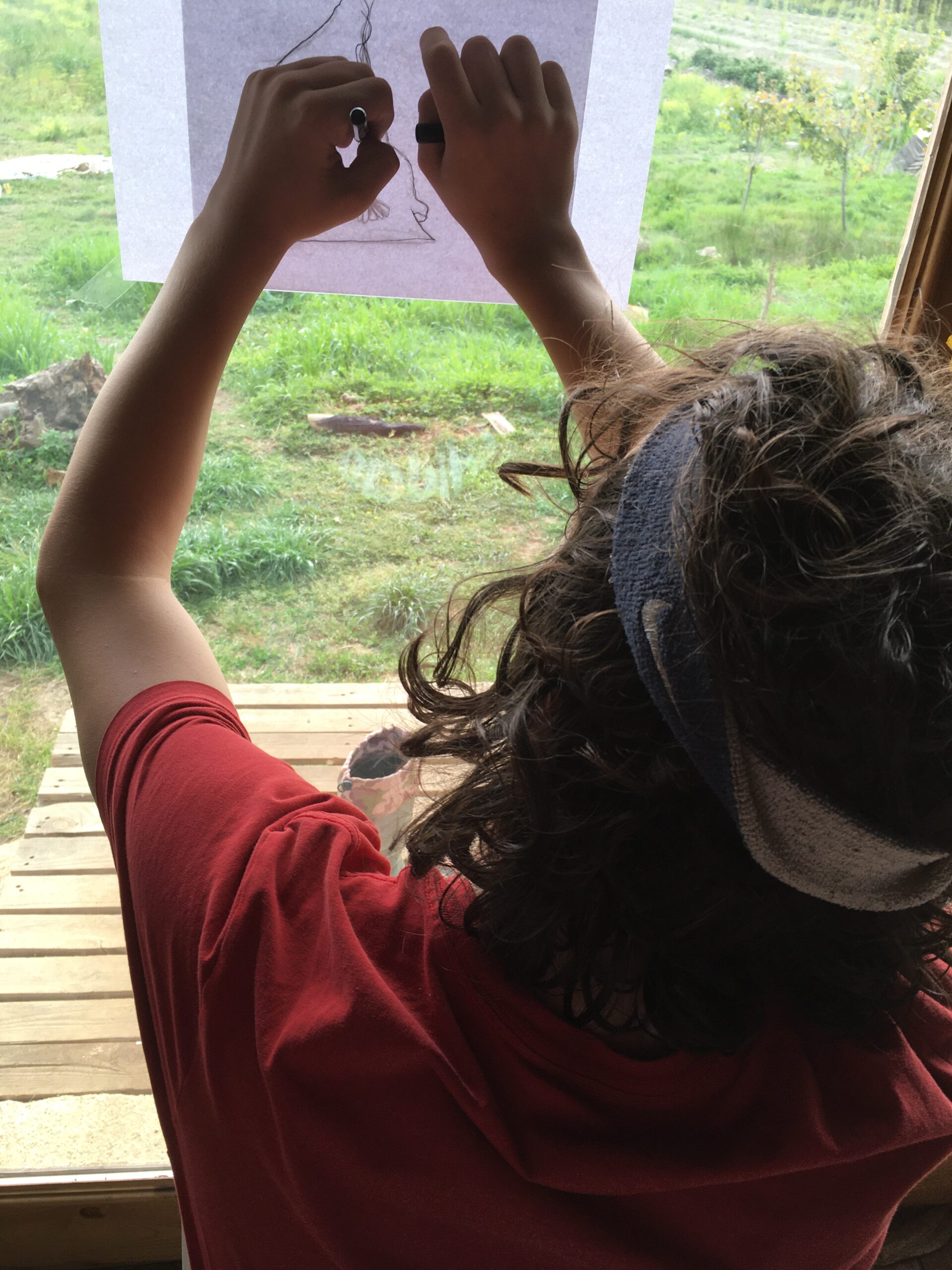 Child holding up a drawing to natural light through a window while working independently at home